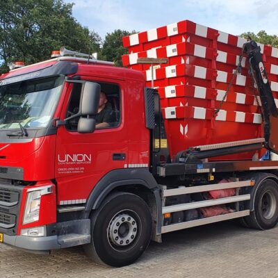 Een partij rood-wit gestreepte portaalarmcontainers op een vrachtwagen.