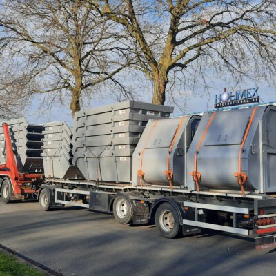 Een vrachtwagen met oplegger waar een grote partij grijze containers mee wordt vervoerd.