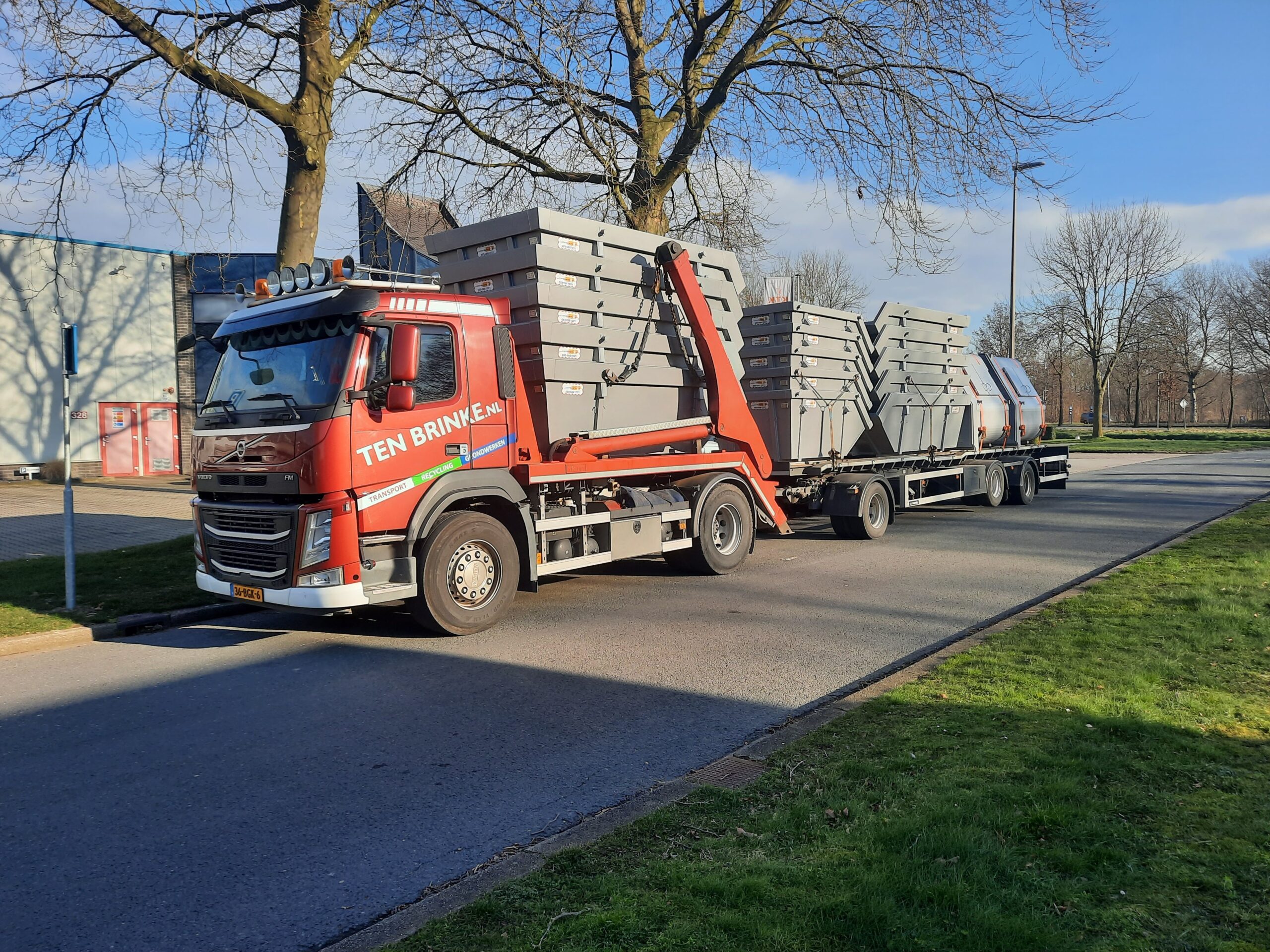 Een vrachtwagen met oplegger waar een grote partij grijze containers mee wordt vervoerd.